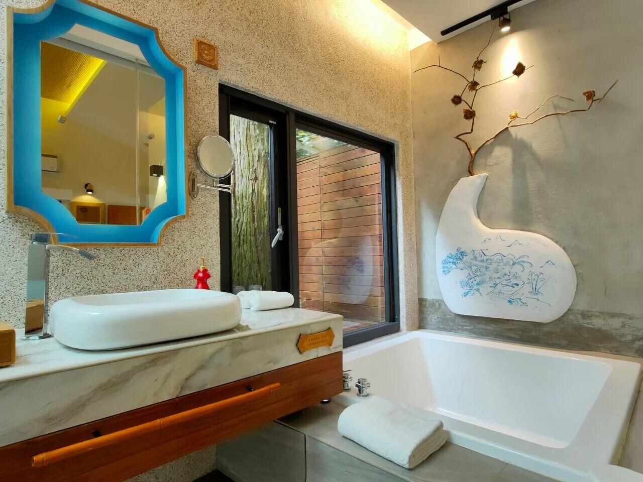 A modern bathroom with a marble vanity, a large mirror, a bathtub, and a decorative wall piece.