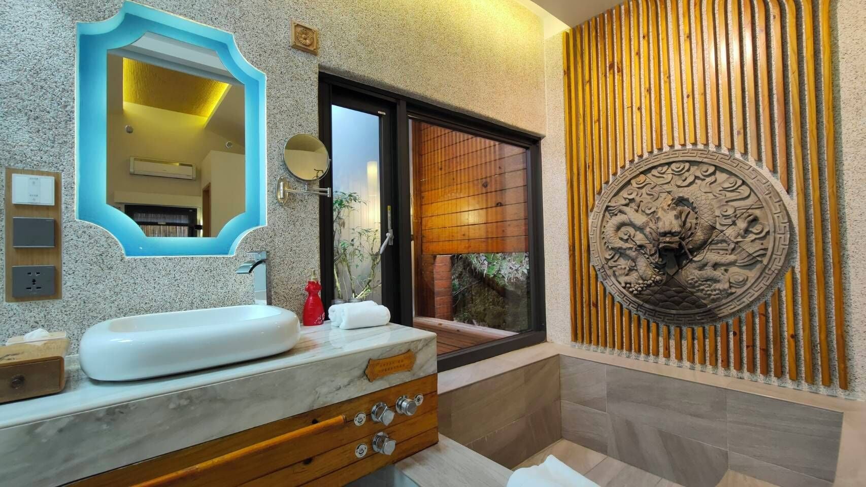 A bathroom with a marble vanity, a round mirror, a wooden door, and a decorative wall panel.