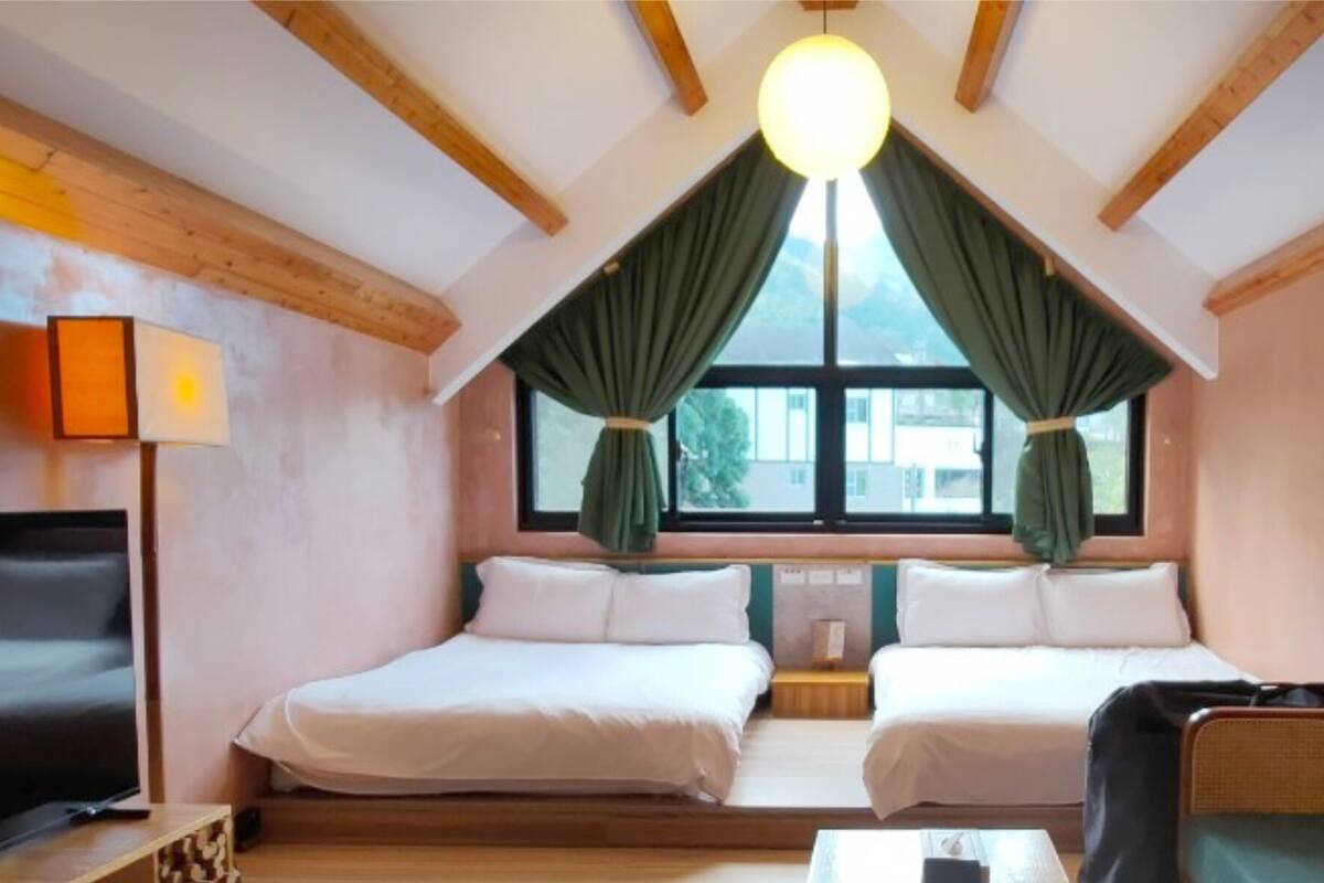 A room with two beds, a TV, a sofa, and a large window with curtains.