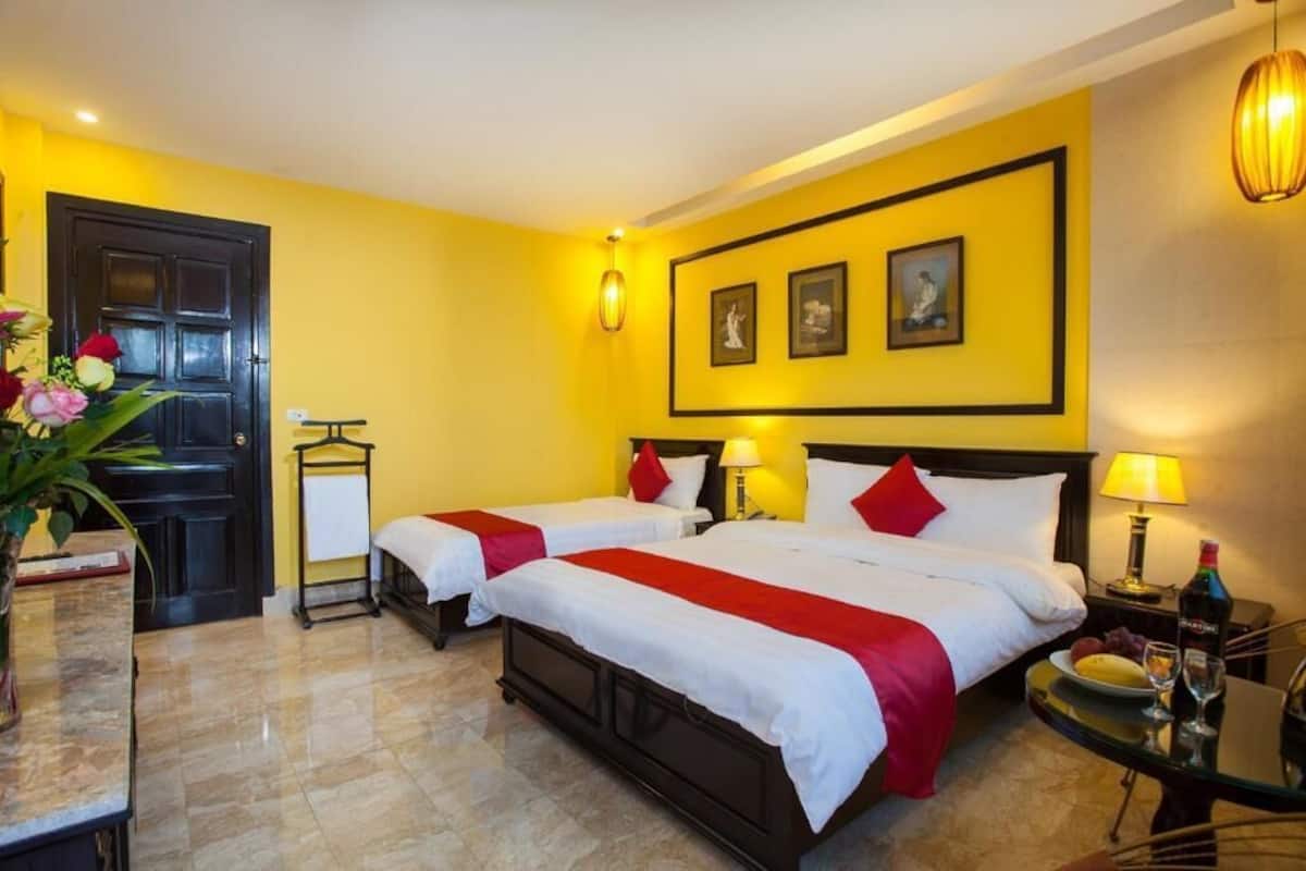 Habitación de hotel con dos camas, una puerta negra, una mesita con una botella y un vaso, y una pared con cuadros enmarcados.
