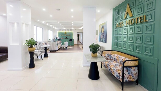 Un hall d’hôtel comprenant un comptoir d’accueil, un espace salon et un mur végétal orné du nom de l’hôtel.