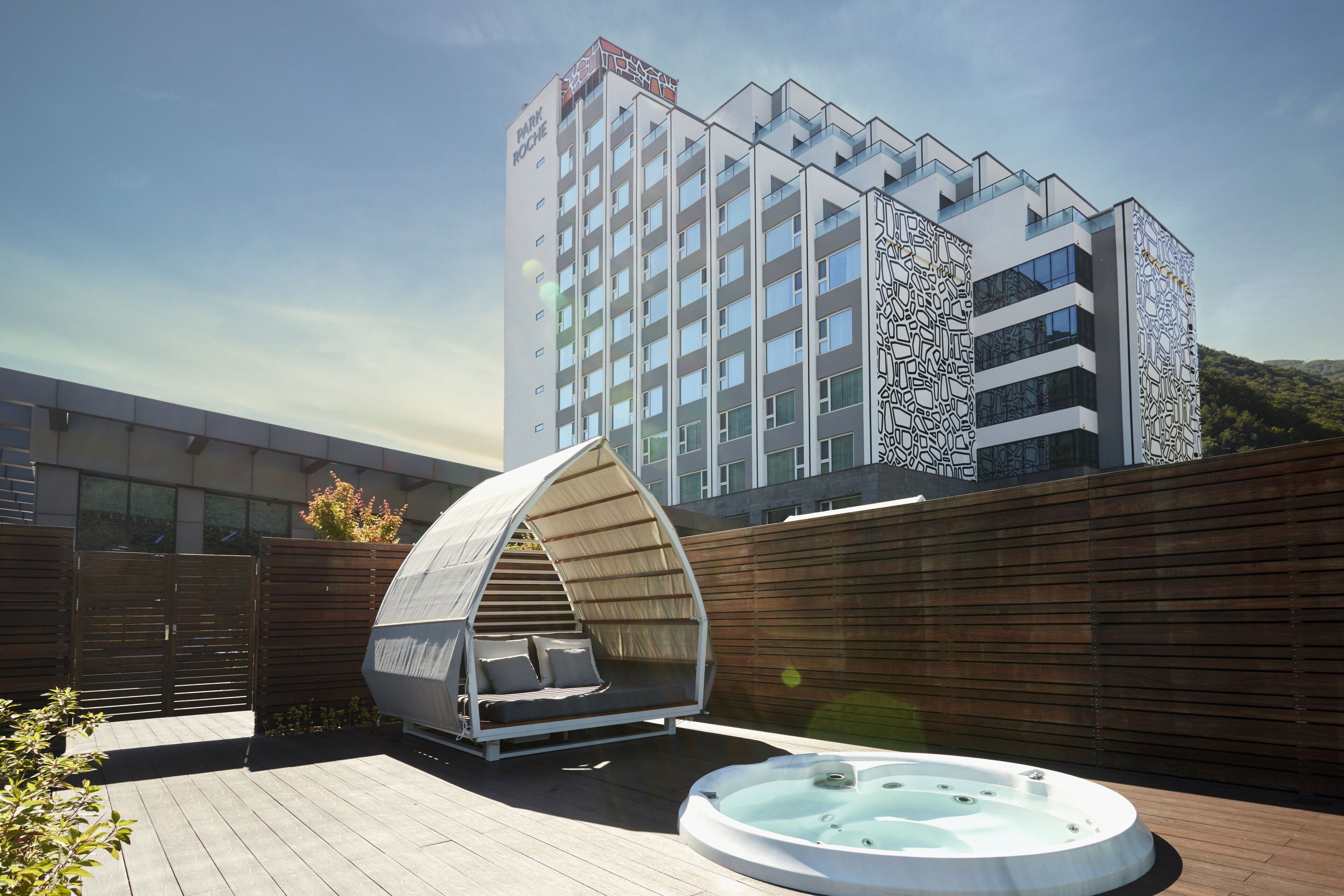 A modern hotel with a rooftop garden, a hot tub, and a unique tent-like structure.