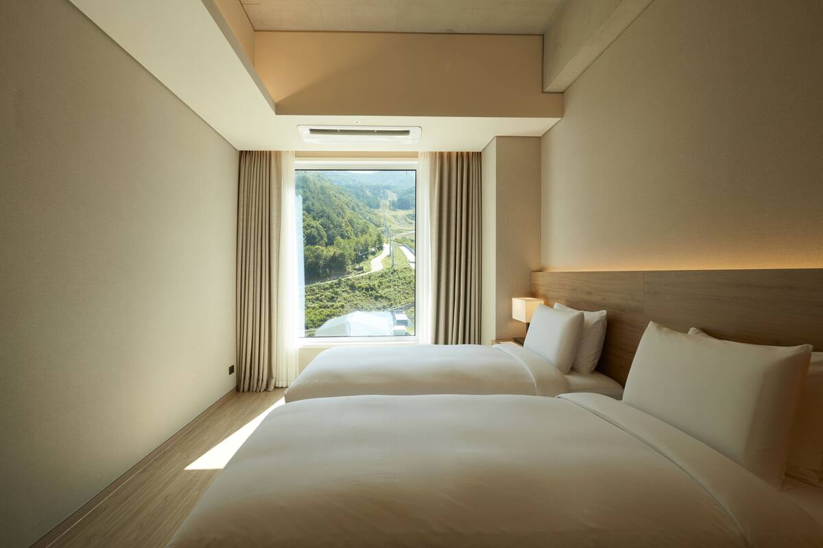 A hotel room with a large bed, a window with curtains, and a view of a green landscape.