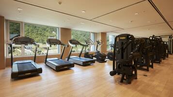 Un gimnasio con cintas de correr y máquinas de pesas, ventanas amplias y suelo de madera.