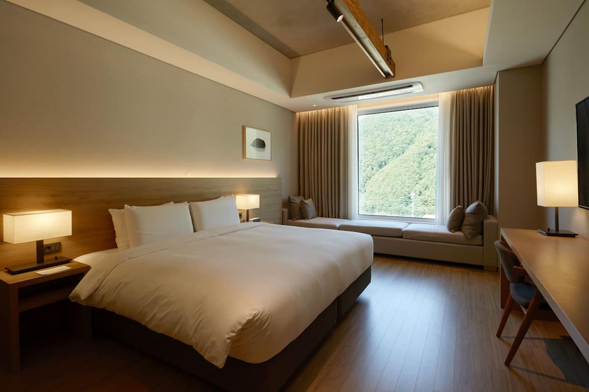 A modern hotel room with a large bed, a desk, and a window with curtains.