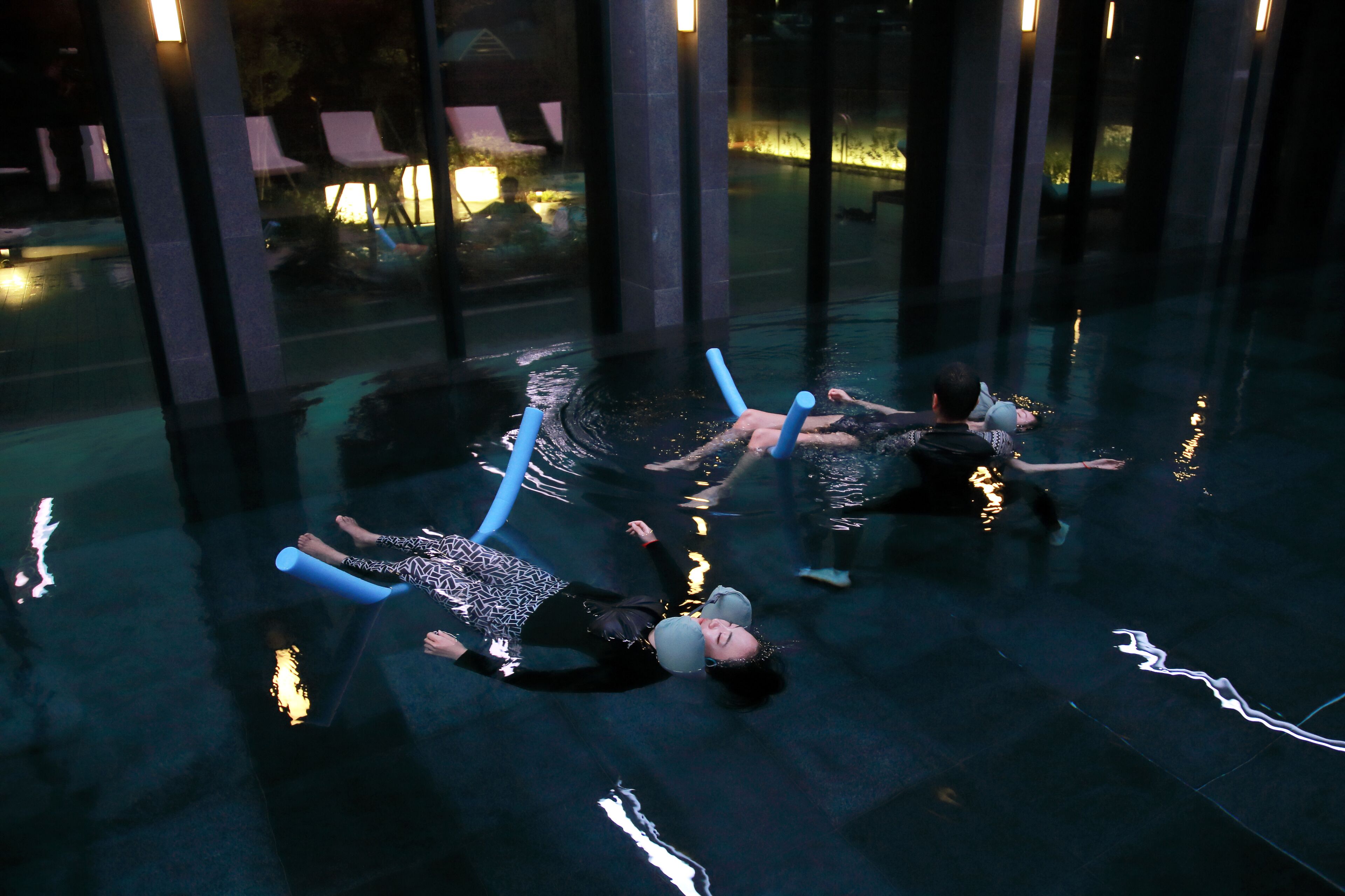 A pool area with people floating on water, surrounded by pillars and glass walls.