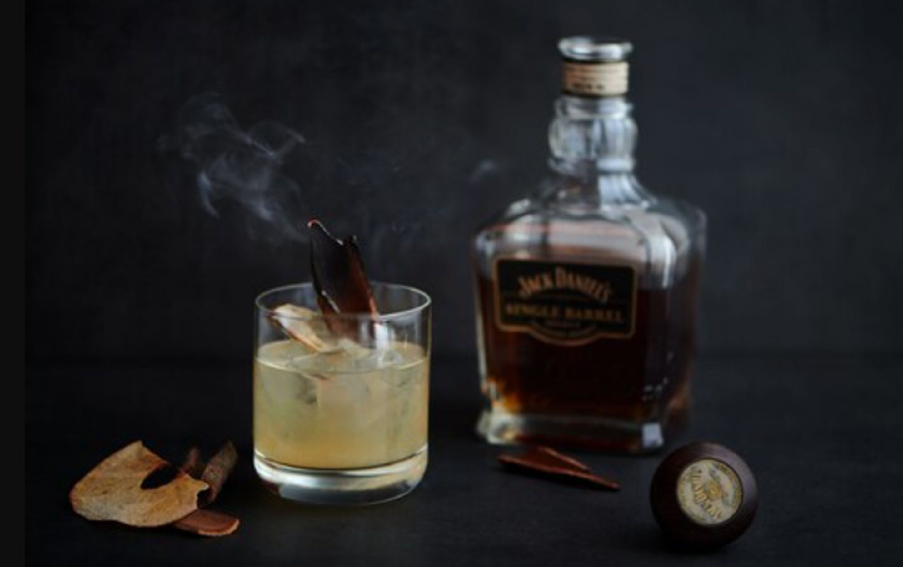 Un vaso de whisky con un bastón de chocolate, una botella de whisky y un barril de madera.