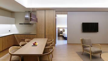 Una habitación de hotel moderna con una mesa de comedor de madera, sillas, un televisor de pantalla plana y una zona de descanso separada con una cama.