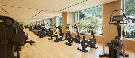 A gym with cardio machines, weight equipment, and large windows offering a view of greenery.