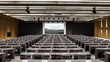 A conference room with rows of tables and chairs, a large screen at the front, and a wooden wall.