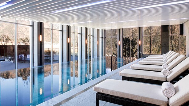 A modern indoor pool area with lounge chairs and a glass-enclosed pool.