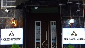 La entrada del AddressSuiteHotel, con una puerta marrón oscuro, dos plantas en macetas y un toldo negro.