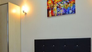 Una habitación de hotel con una cama, almohadas blancas, una colcha marrón y un cuadro de colores en la pared.