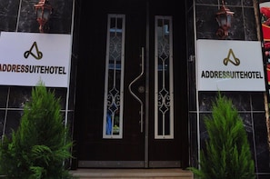 The entrance to AddressSuiteHotel with a dark facade, two symmetrical doors with decorative metalwork, and potted plants at the entrance. - AddresSuitesHotel (Istanbul)