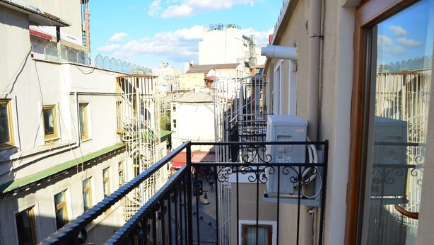 Una calle urbana estrecha con edificios a ambos lados, una barandilla metálica y un cielo despejado.