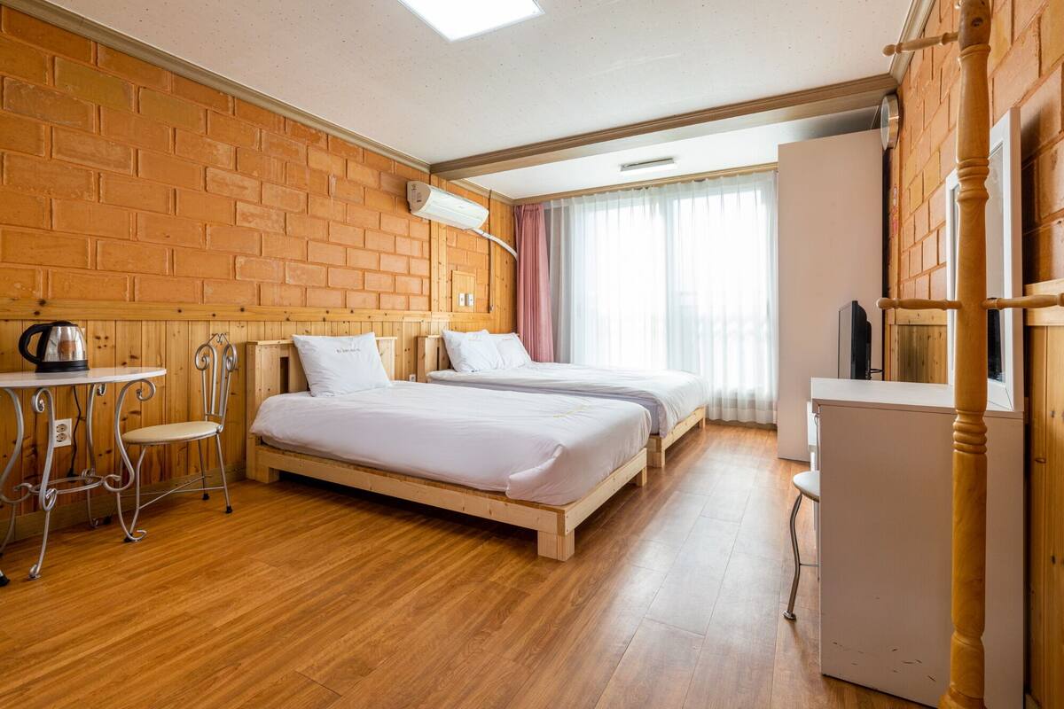 A hotel room with two wooden beds, a small table with a kettle, a chair, and a wooden wardrobe.