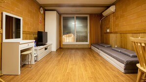 A room with a wooden floor, a TV on a white cabinet, a sofa, and a window with curtains. - Red Clay (Jeju City)