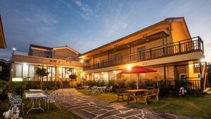 A two-story building with a brick facade, outdoor seating area with tables and chairs, and a staircase leading to the upper level. - Red Clay (Jeju City)