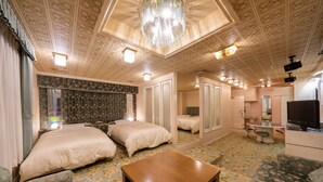 Een hotelkamer met twee bedden, een houten tafel, een bank, een spiegel, een televisie en een plafond met gedetailleerde patronen.