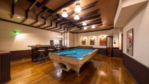 Een pooltafel in een ruimte met houten vloeren, een bar en kunstwerken in lijsten aan de wanden.