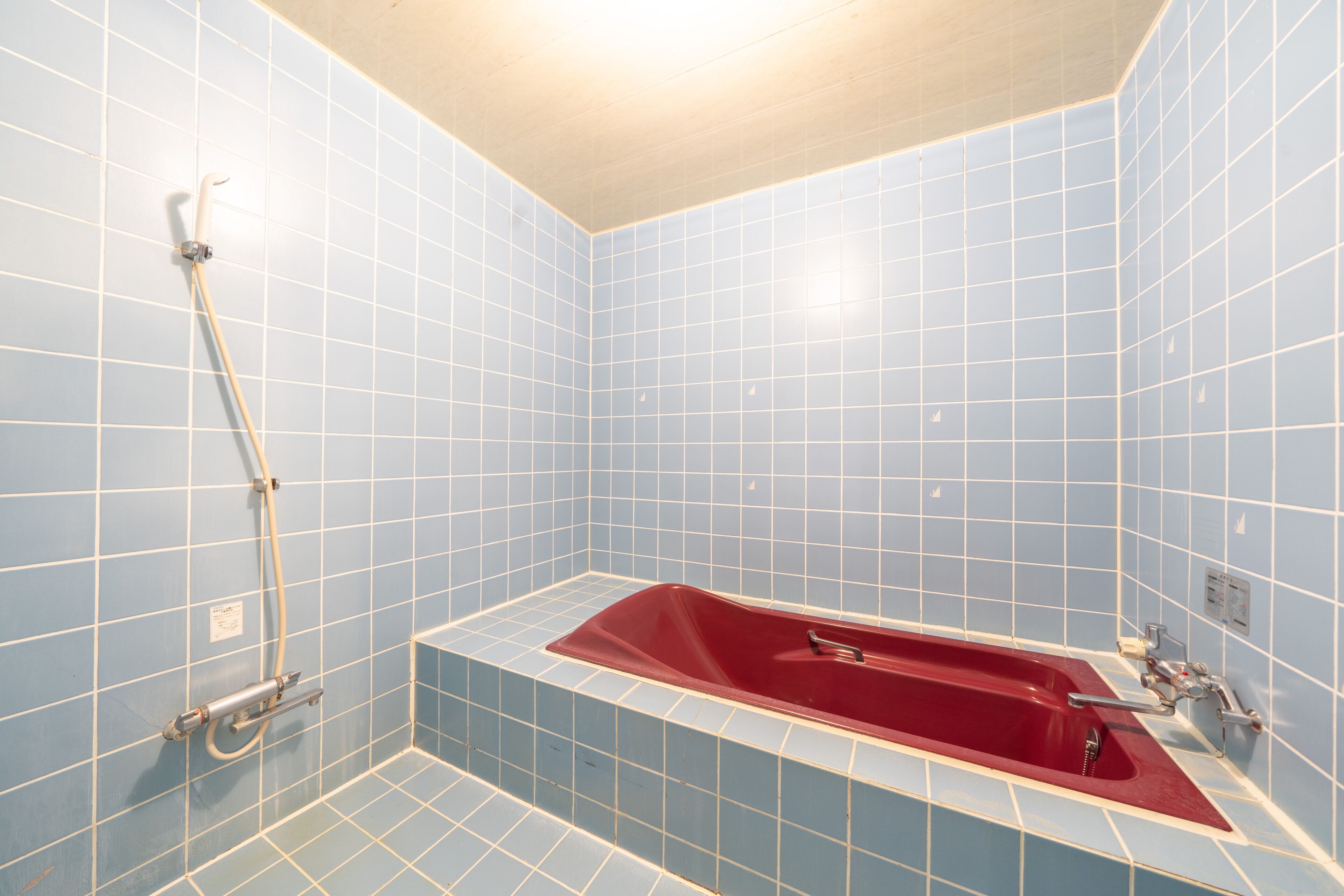 A bathroom with blue tiled walls, a red bathtub, and a showerhead.