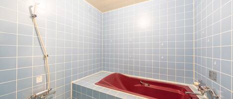 A bathroom with blue tiled walls, a red bathtub, and a showerhead.