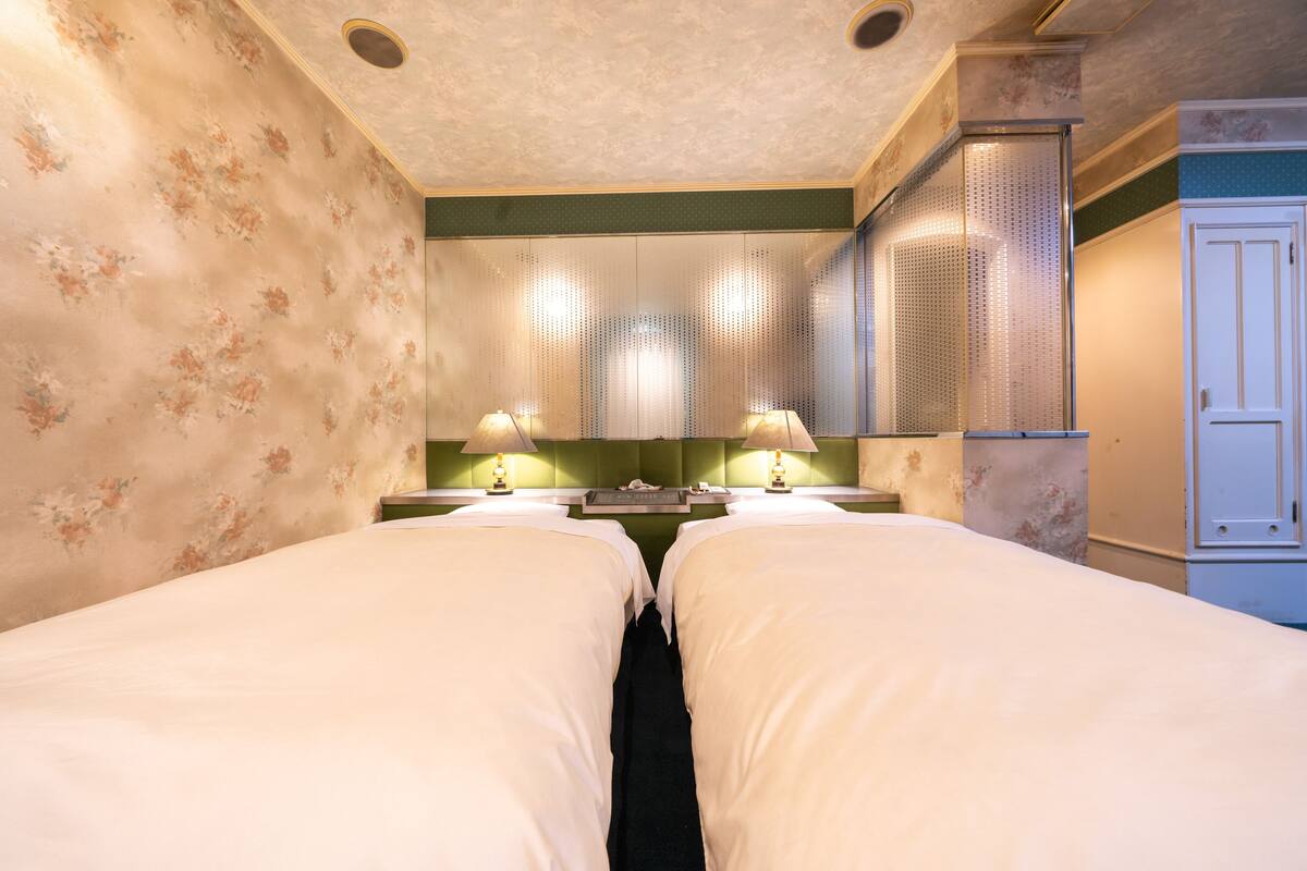 Ein Hotelzimmer mit zwei Betten, einer grünen Akzentwand und einem Schrank mit Spiegel.