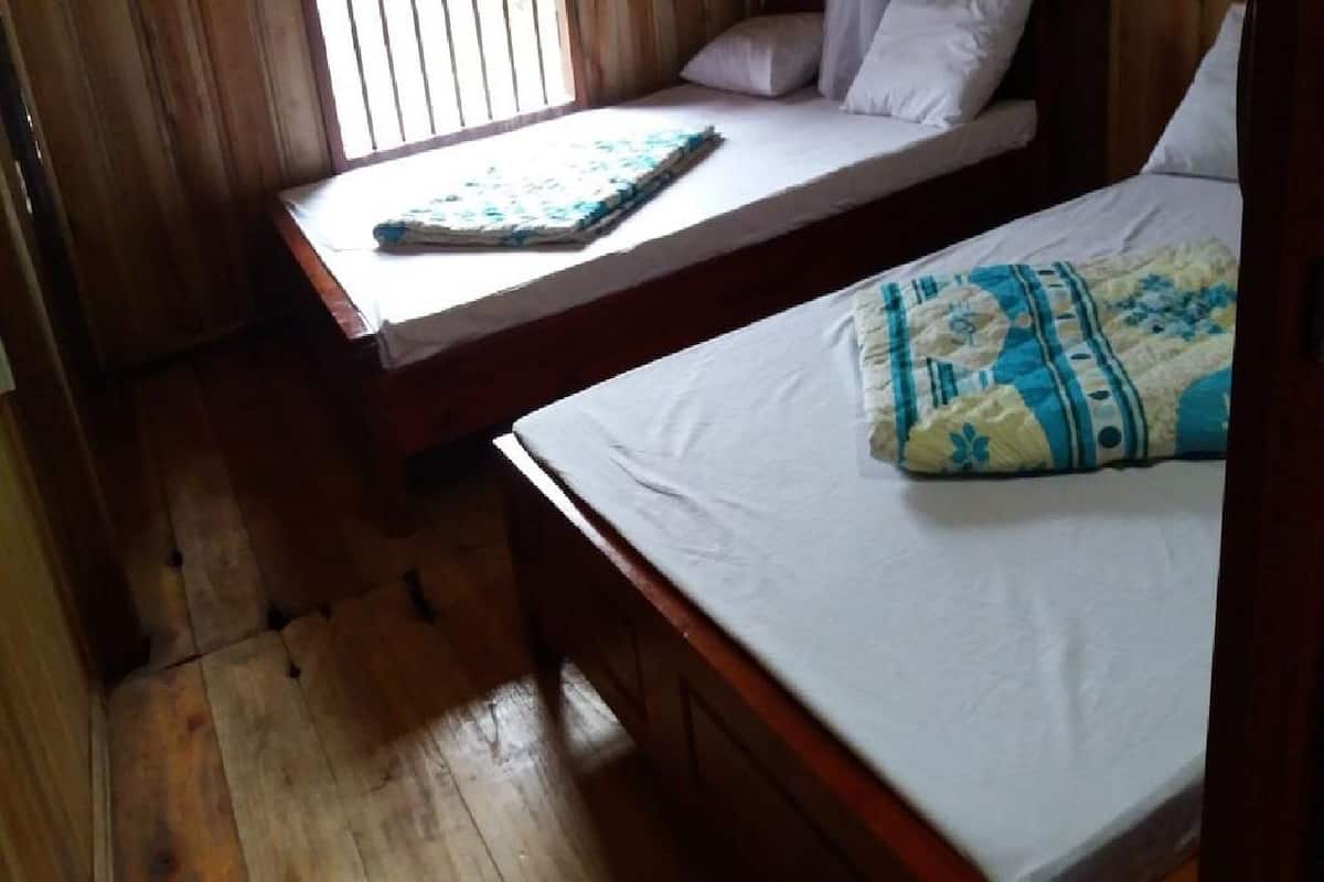 A room with two wooden beds, one with a blue and white patterned bedspread and the other with a plain white bedspread.