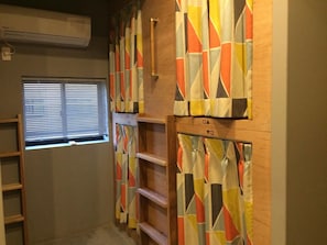 Quarto com beliches, janela com persianas e estante de madeira com compartimentos identificados.