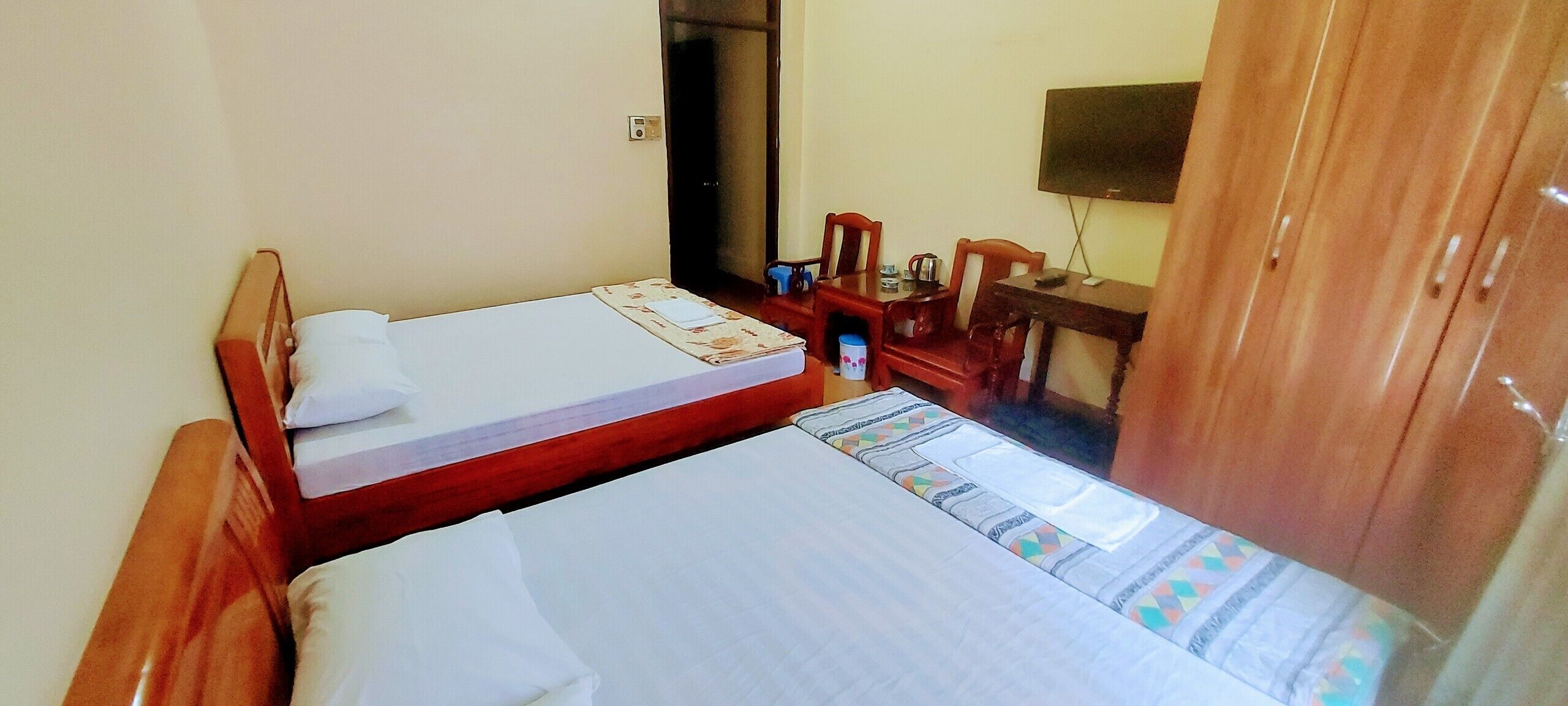 A hotel room with two single beds, a wooden desk, a chair, a television, and a wardrobe.