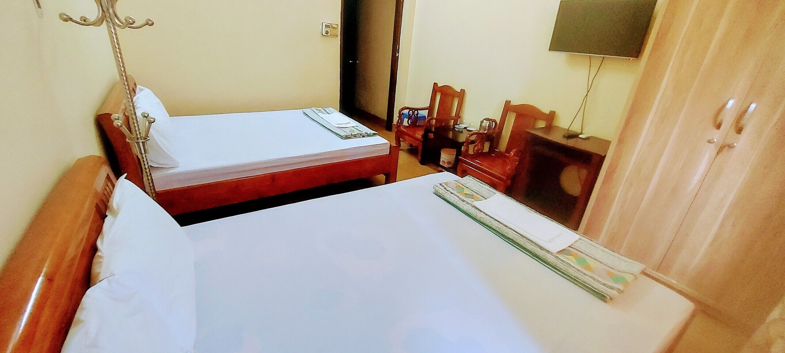 A hotel room with two beds, wooden furniture, a TV, and a wardrobe.