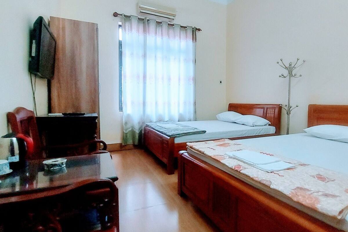 A hotel room with two beds, a desk with a chair, a television, and a coat rack.