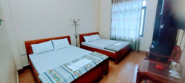 A room with two single beds, a wooden floor, a coat rack, and a window with curtains.