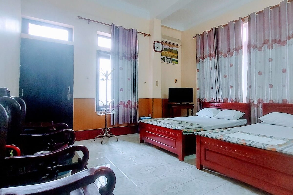 A hotel room with two beds, a TV, a desk with a chair, and a wardrobe.
