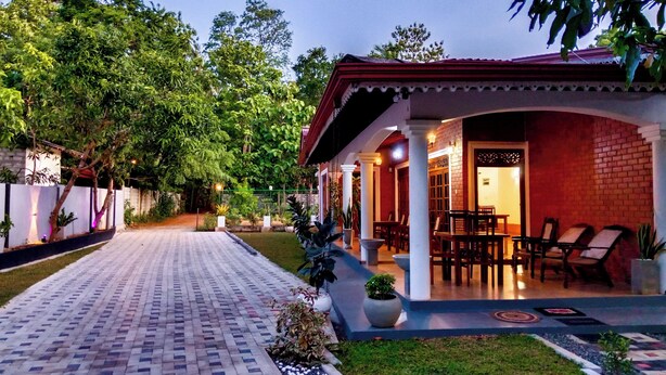 A covered outdoor seating area with tables and chairs, a brick wall, and potted plants. - Sigiri Thilanka Rest (Sigiriya)