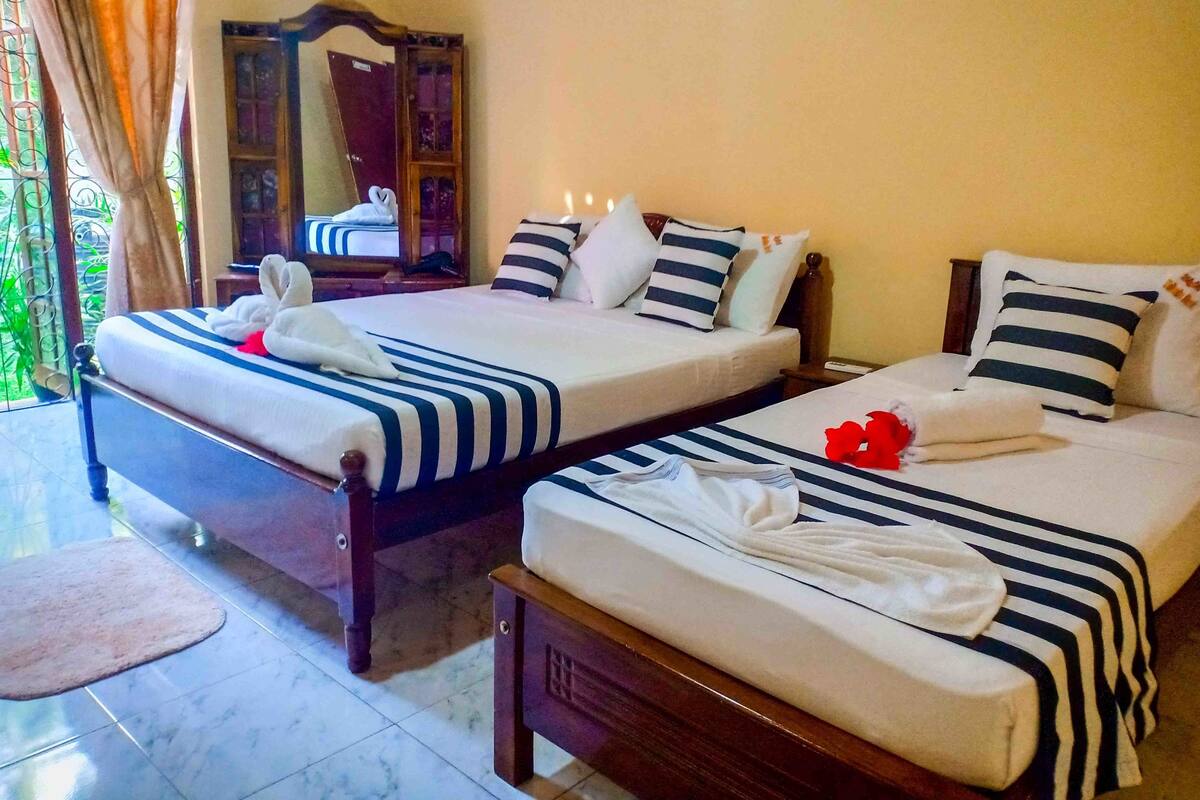 Two double beds with striped bedding, a wooden nightstand, a mirror, and a window with curtains.