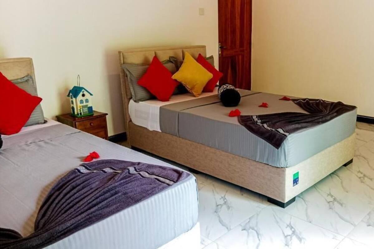 A hotel room with two beds, a nightstand, a small decorative birdhouse, and a red curtain.