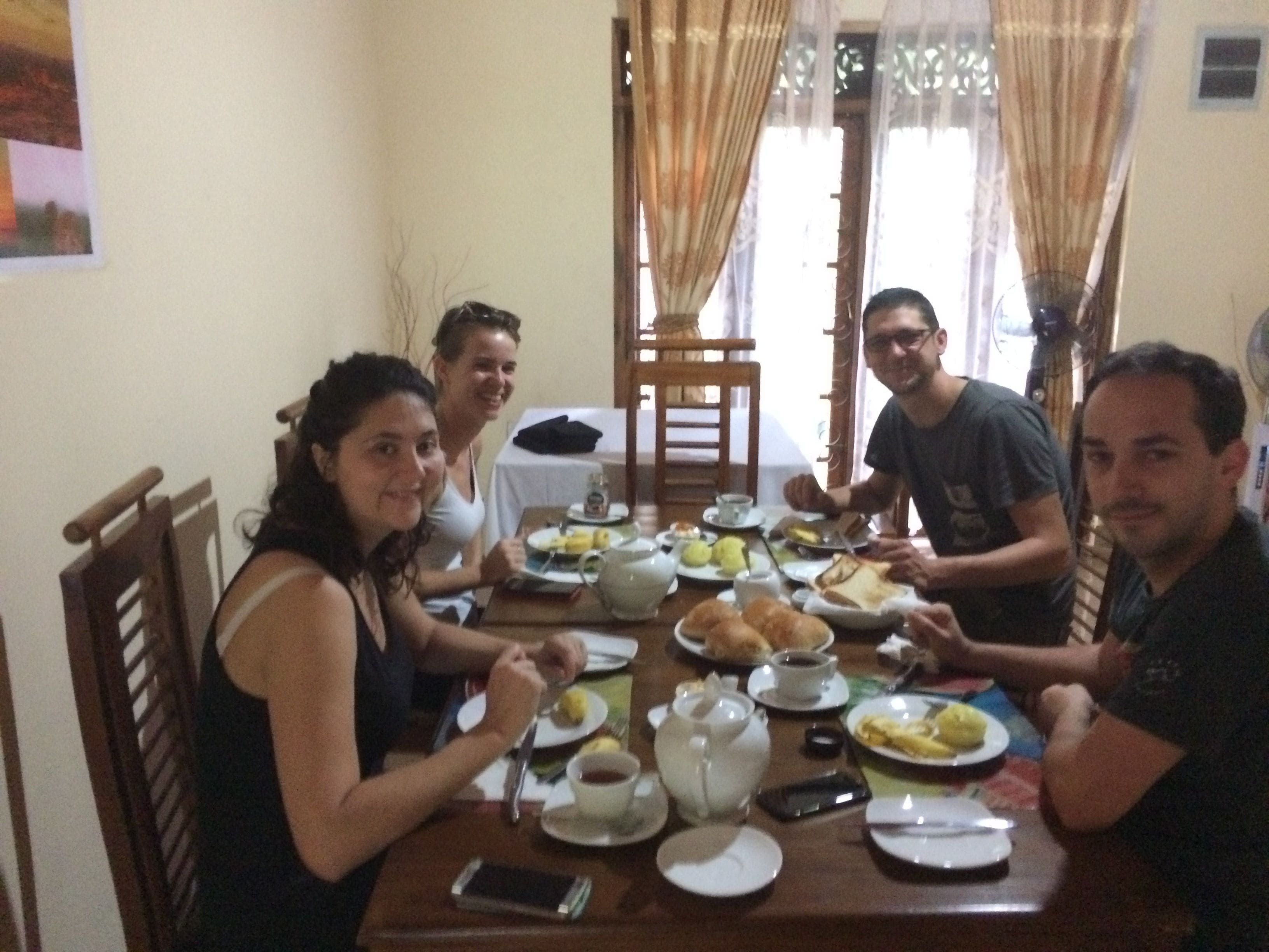 A group of people dining at a wooden table with various dishes and a teapot.