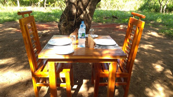 A wooden picnic table with four chairs, set outdoors with a tree in the background.
