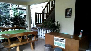 Een houten receptiebalie met een bord waarop staat 'BUNAKIDZ LODGE INFORMATION' en een houten bank ervoor.