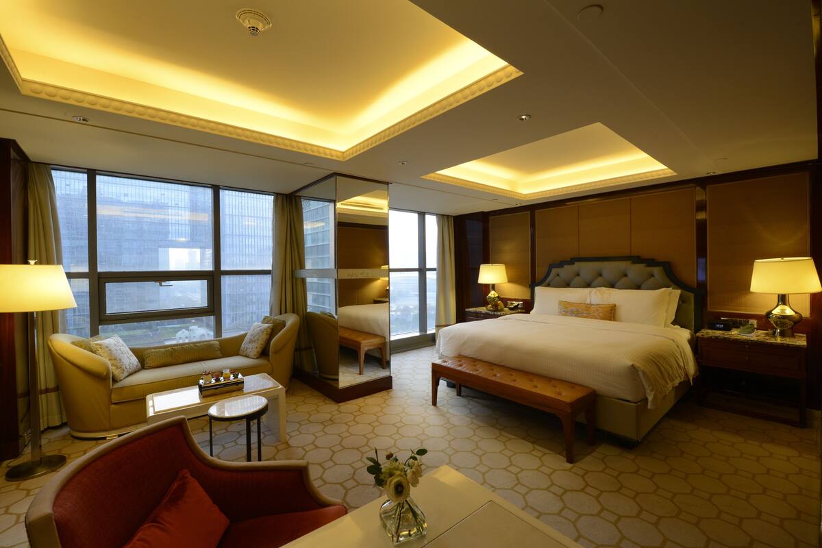 Una habitación de hotel con una cama grande, un sofá, una mesita y un espejo.