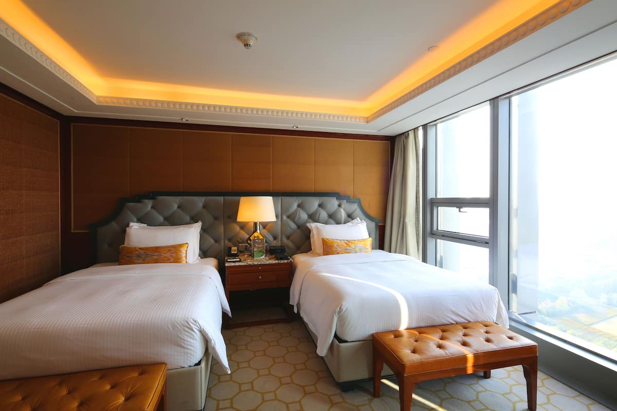 Habitación de hotel con dos camas, un ventanal grande y vista a la ciudad.