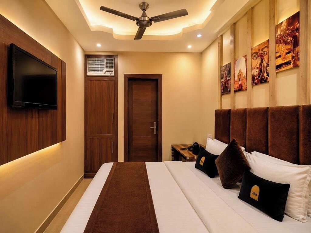 Habitación de hotel con cama, televisión, ventilador de techo y obras de arte en las paredes.