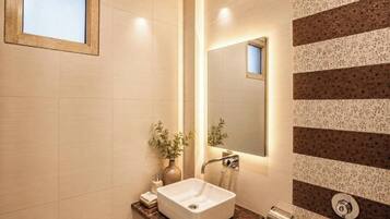 Une salle de bain avec un lavabo blanc, un miroir, un distributeur de serviettes et un mur à motifs rayés.