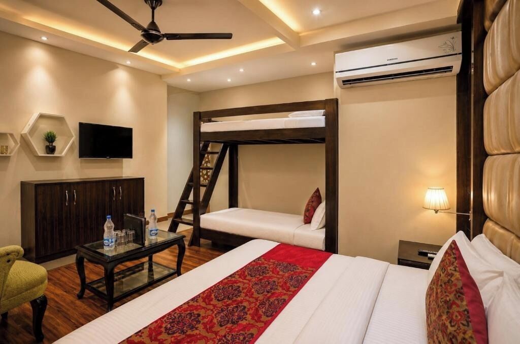Habitación de hotel con literas, un televisor de pantalla plana, un escritorio con botellas de agua, un sofá y una lámpara.