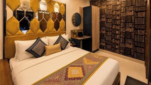Habitación de hotel con una cama grande, un ventilador de techo, un escritorio con una computadora portátil y una estantería.