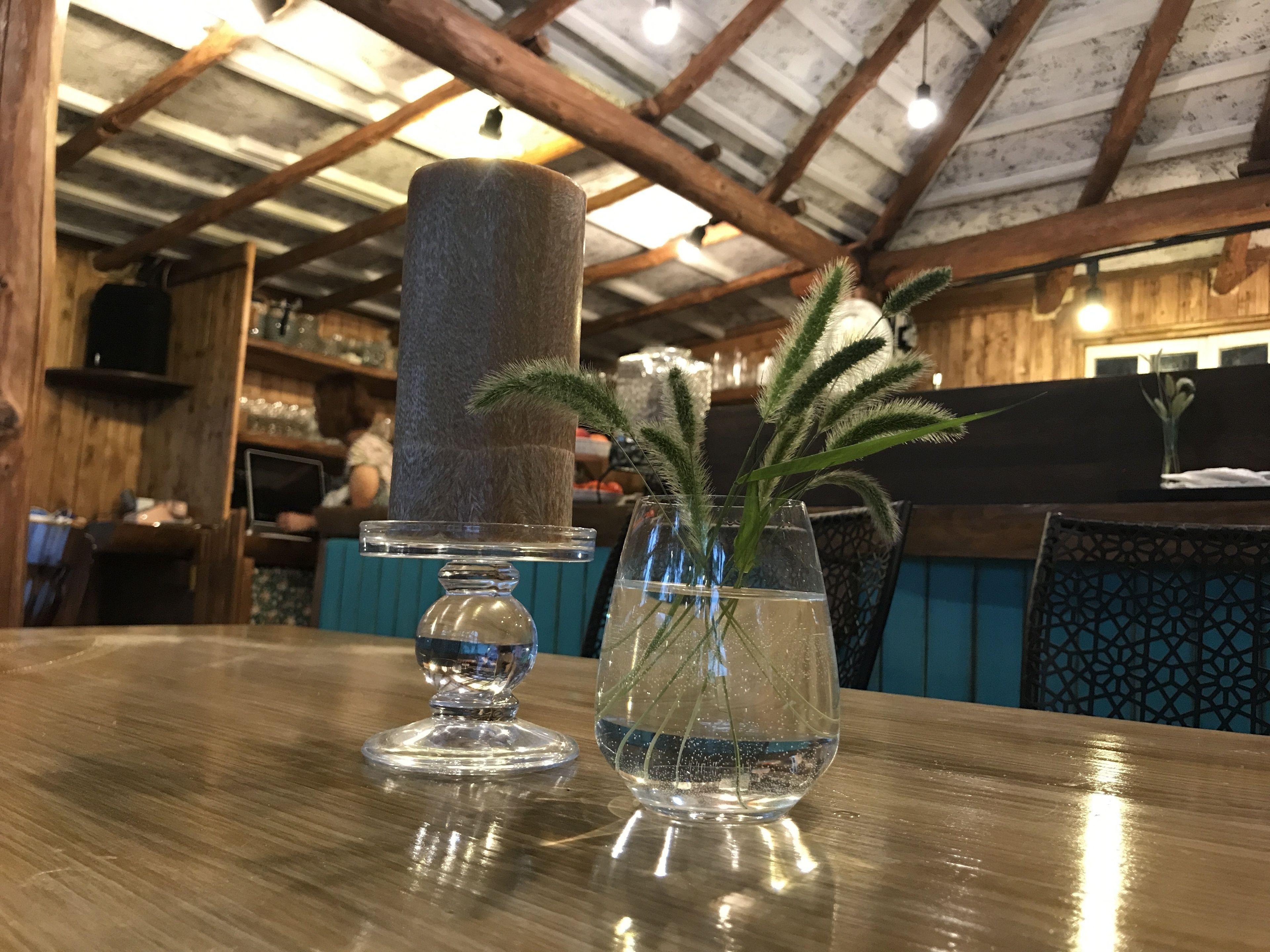 A wooden table with a clear glass vase containing a plant and a clear glass candle holder.