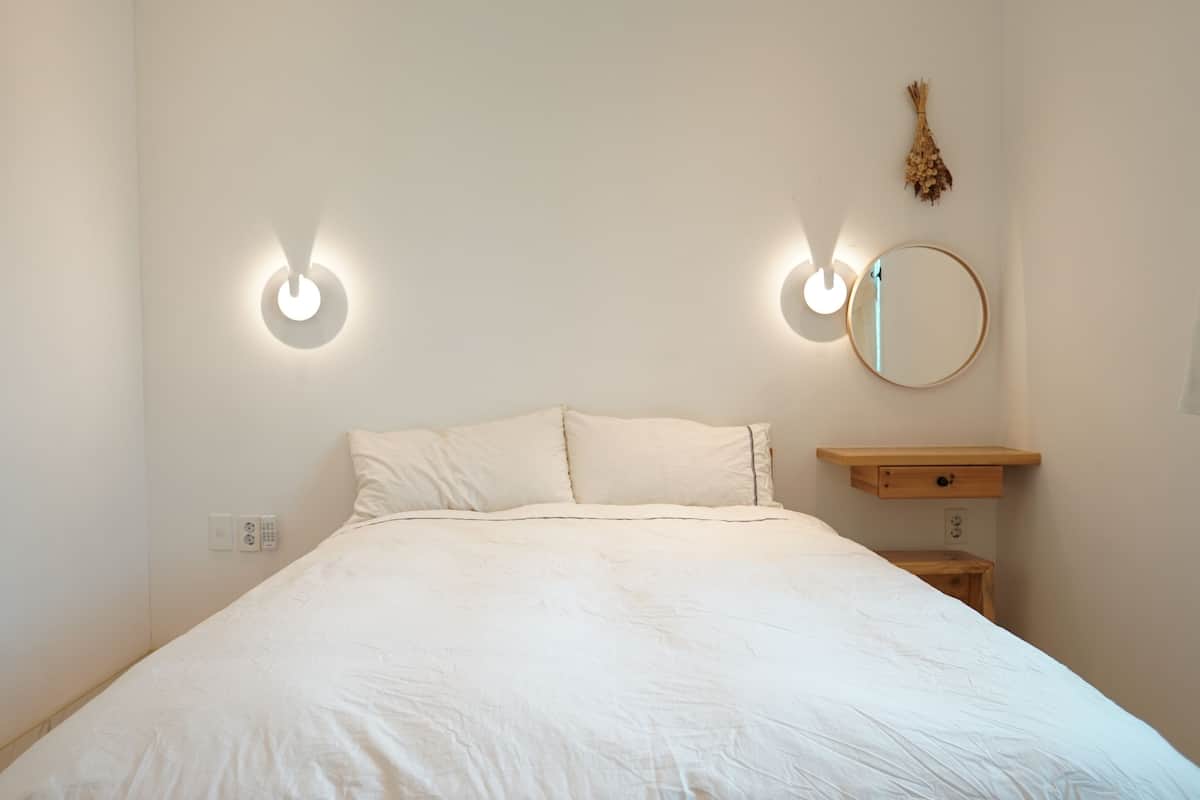 A minimalist bedroom with a large bed, two wall-mounted lights, a bedside table, and a mirror.