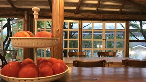 A wooden dining table with a bowl of oranges and a colander with oranges.