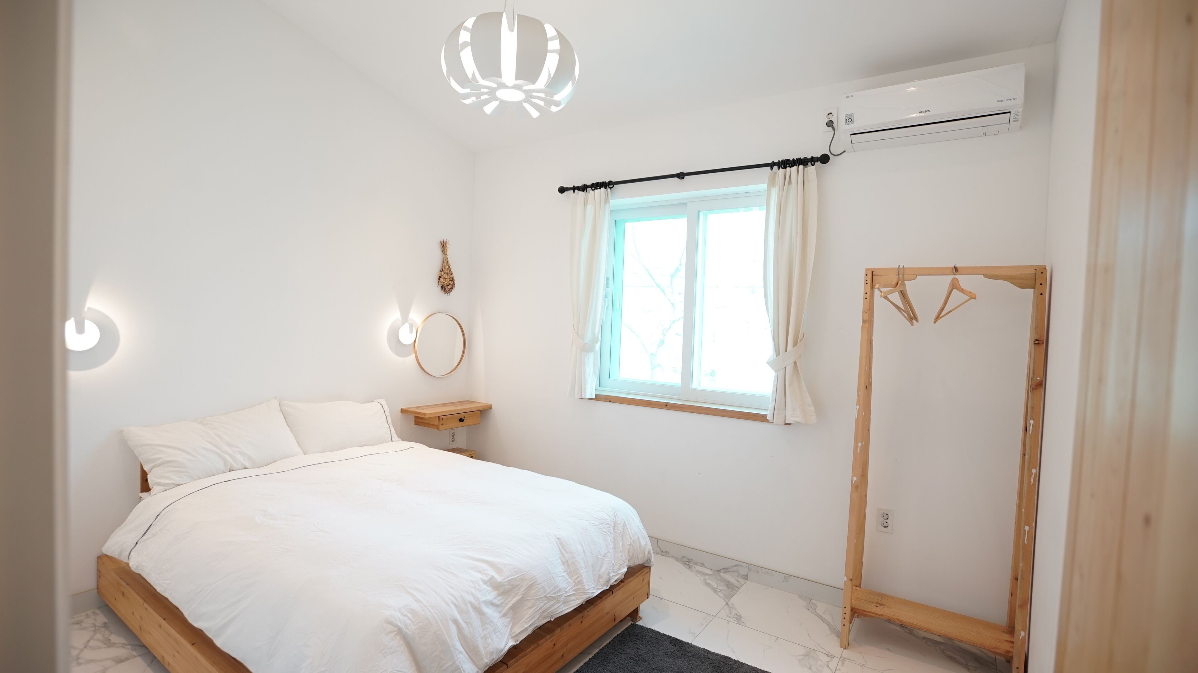 A bedroom with a bed, a bedside table, a hanging light fixture, a window with curtains, and a wooden wardrobe.